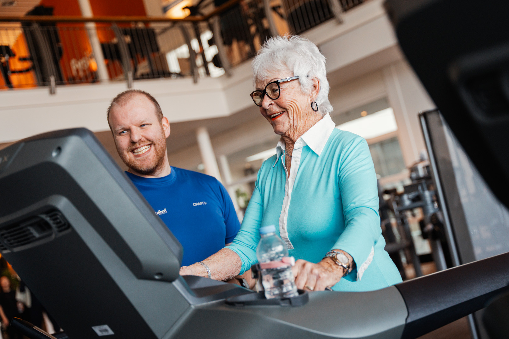 Instructeur personal trainer fitnesscoach die een oudere dame begeleidt op een loopband